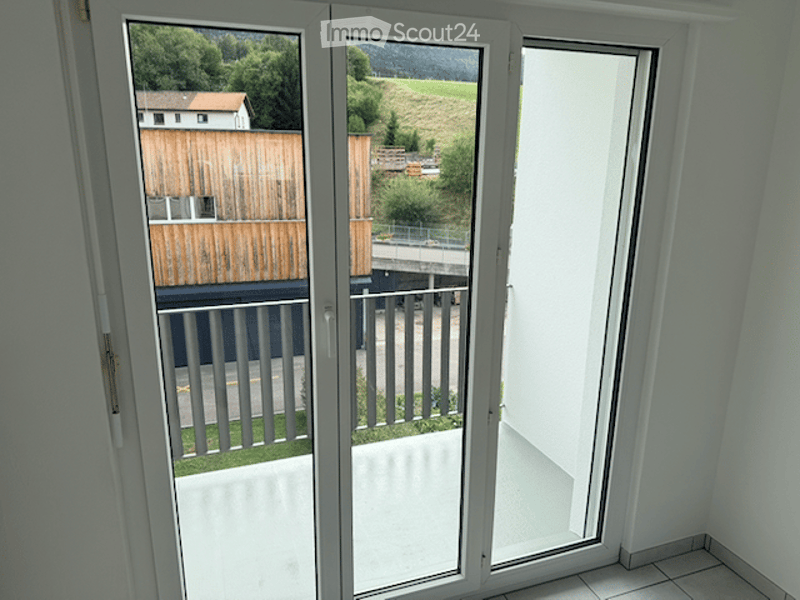 Balcony with large glass sliding doors, metal railing, and scenic view of greenery and a road.