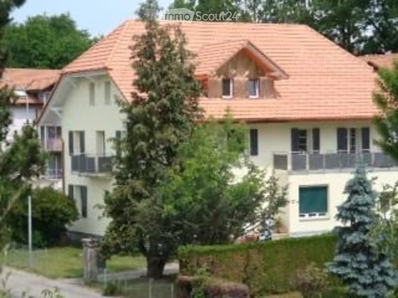 Two-story house with a red-tiled roof, white walls, multiple windows, and balconies. Surrounded by greenery and trees.
