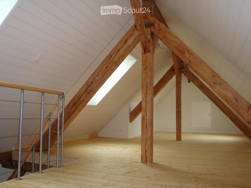 Empty attic space with wooden beams, exposed wooden ceiling, skylight window, and wooden floor.