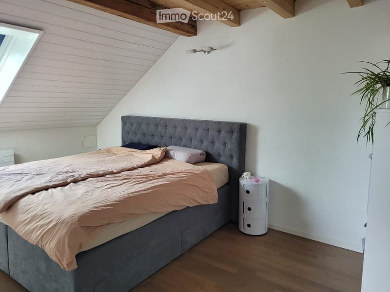 Cozy bedroom with a tufted headboard, beige bedding, wooden floor, and a small white nightstand with a lamp.