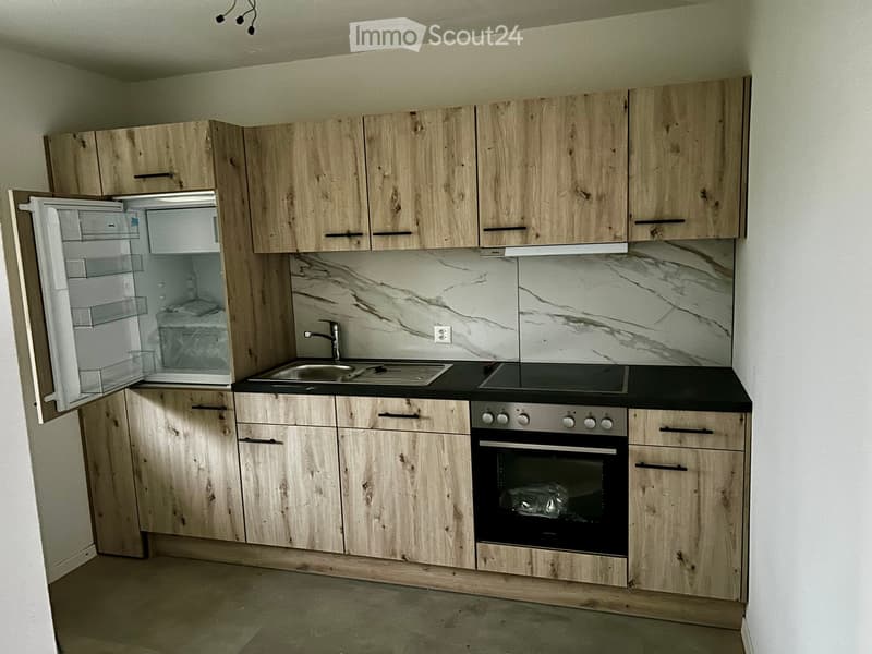 Modern kitchen with light wooden cabinets, marble backsplash, and stainless steel appliances including a refrigerator, sink, and oven.