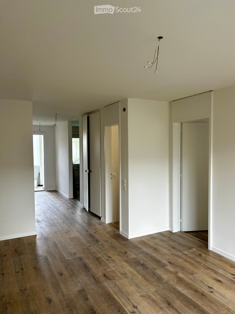 Empty room with hardwood floors, white walls, and two open doors leading to other rooms