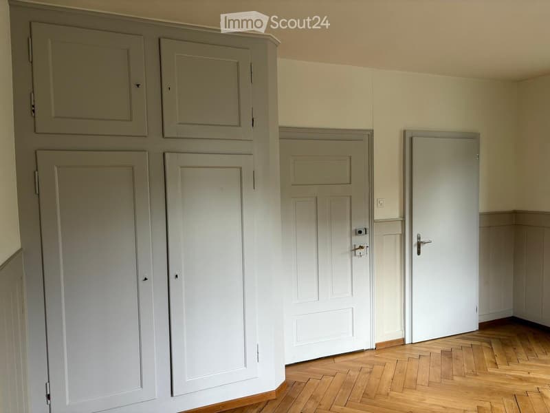 Empty hallway with wooden flooring, multiple doors, and light-colored walls.