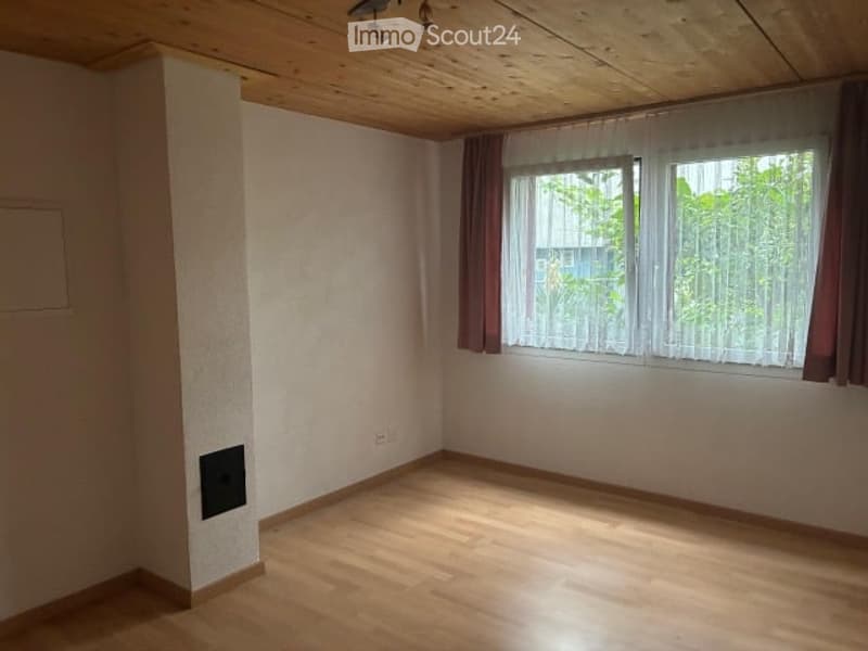 Empty room with wooden flooring, white walls, and large windows with curtains. No furniture or equipment present.