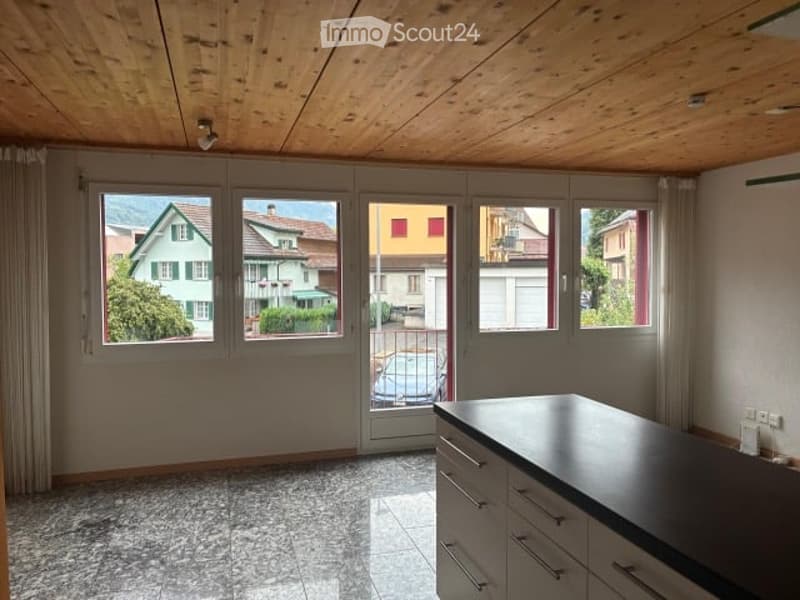 Empty room with wooden ceiling, large windows, and a kitchen counter with drawers. No furniture or equipment present.