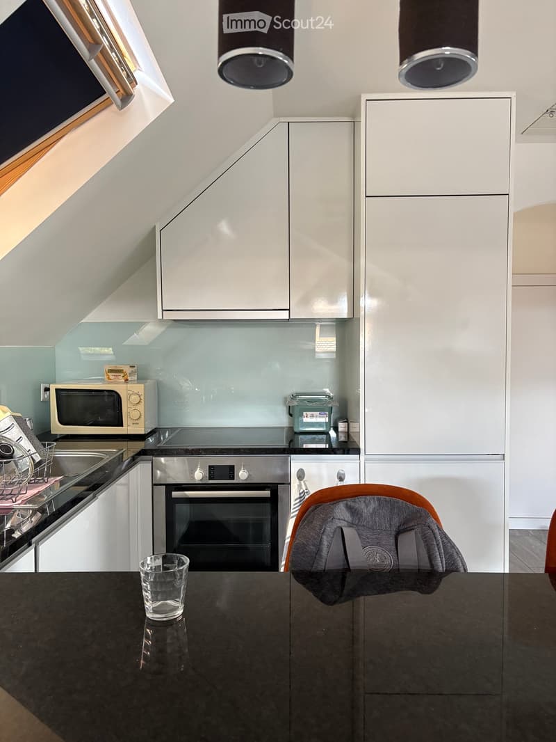 Modern kitchen with white cabinets, stainless steel appliances, and a dark countertop. Features include a microwave, oven, dish rack, and a baby chair at the counter.