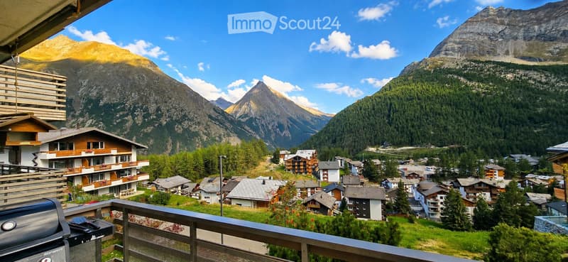 Balcony overlooking a picturesque village with traditional houses and surrounding mountains under a clear blue sky.