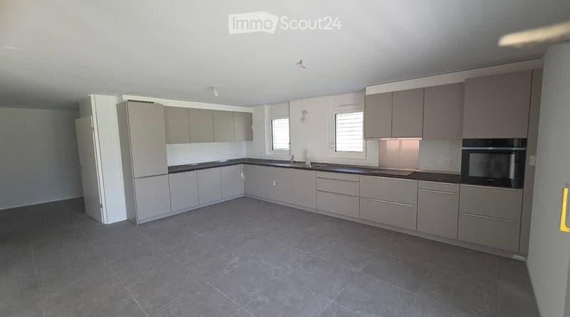 Modern kitchen with grey cabinets, black countertops, and grey tiled flooring. Features include a sink, an oven, and two windows with blinds.