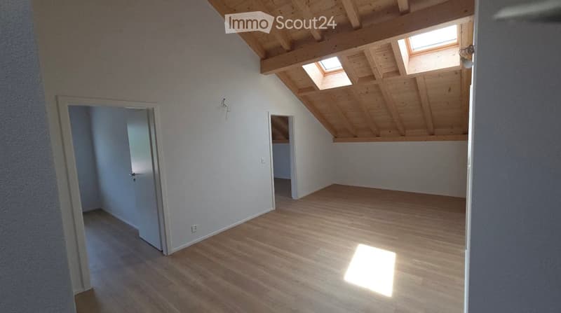 Empty attic room with wooden floor and exposed wooden beams, skylights, and white walls.