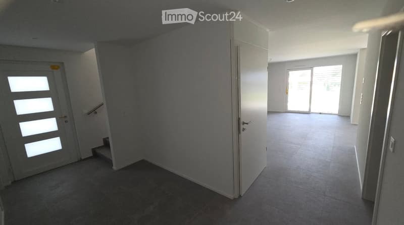Empty hallway with tiled floor, white walls, and a staircase leading upwards. A sliding glass door at the end provides natural light.