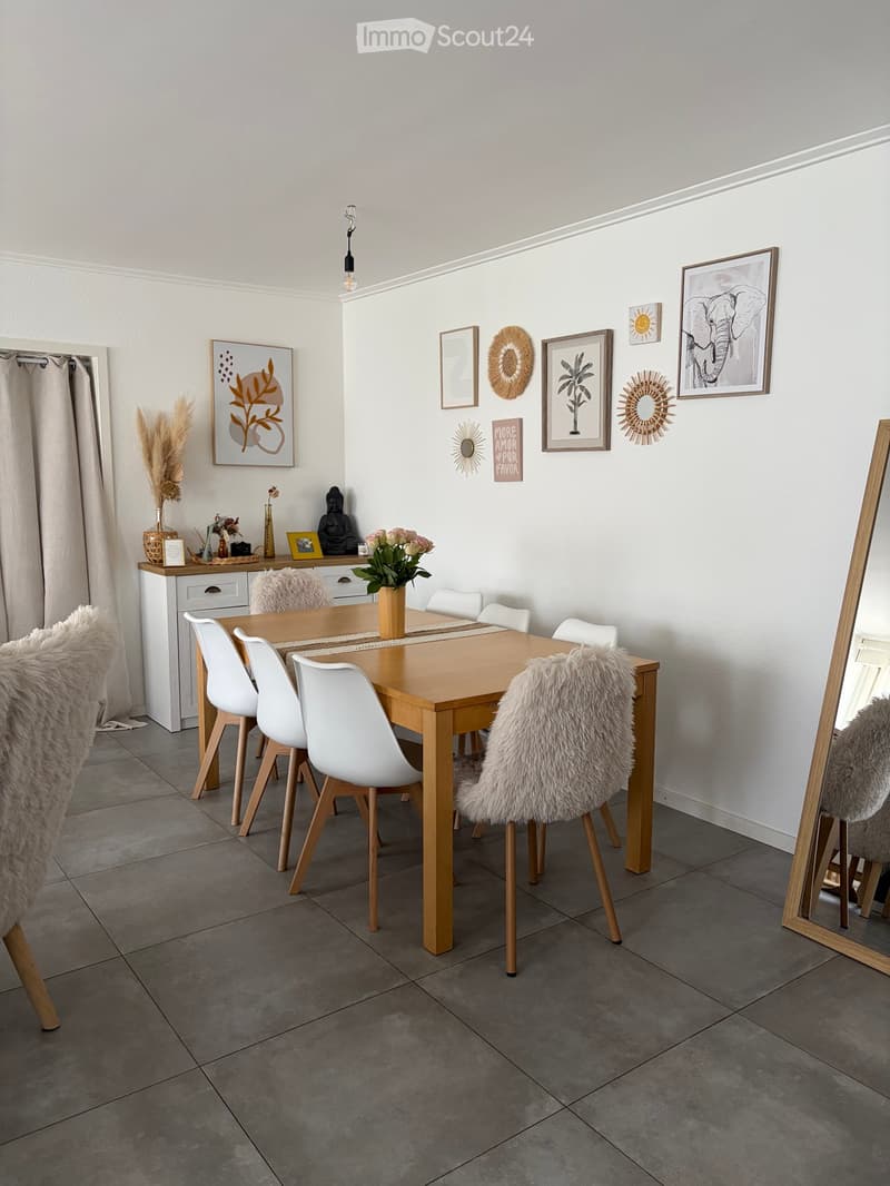 Dining room with a wooden dining table, white chairs, a large mirror, and decorative items on the walls and shelves.