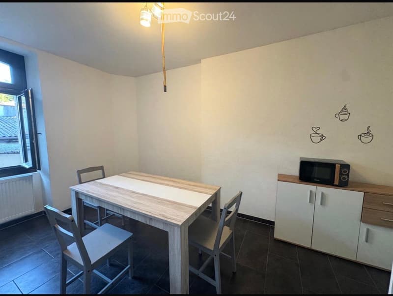 Modern kitchen with a light wooden dining table, four chairs, white cabinets, and a microwave on the counter.