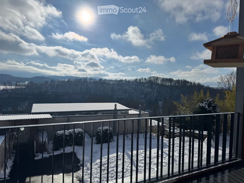 Balcony with metal railing overlooking a snowy landscape and distant hills under a partly cloudy sky.