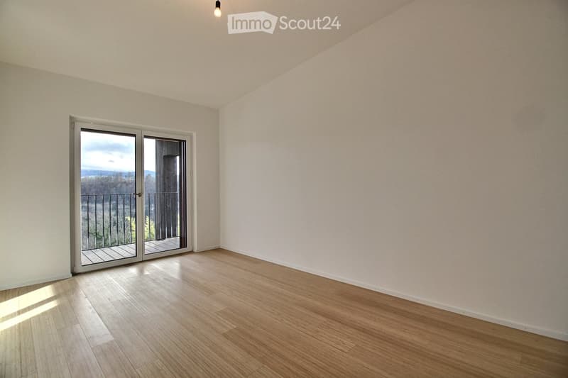 Empty room with light wooden flooring, white walls, and a large sliding glass door leading to a balcony with a scenic view.