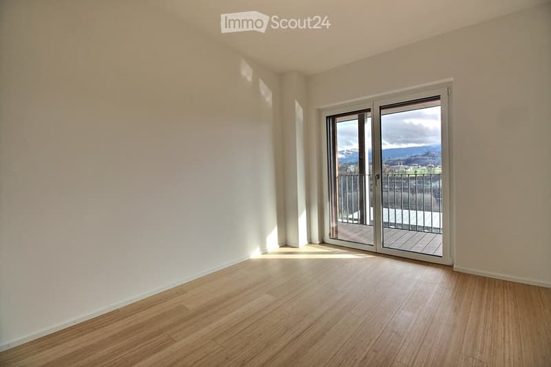 Empty room with light wooden flooring and white walls, featuring a large sliding glass door leading to a balcony with a scenic mountain view.