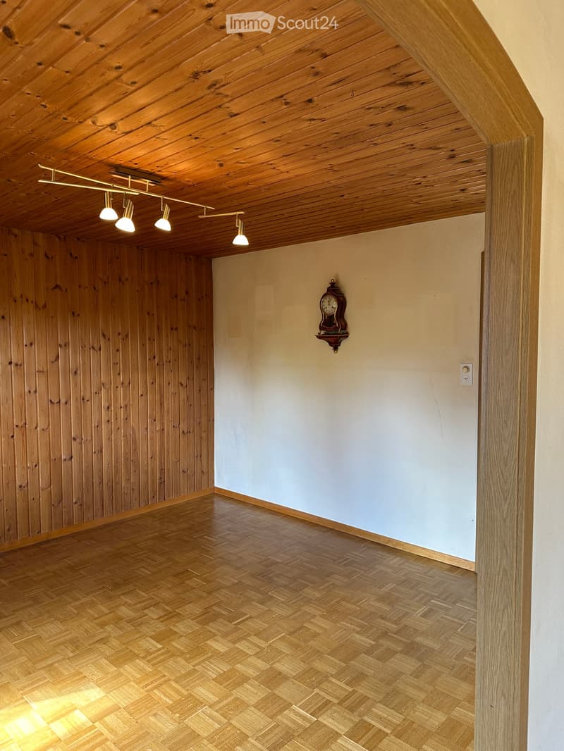 Empty room with wooden walls, herringbone wooden floor, exposed wooden ceiling, track lighting, and a wall-mounted clock.