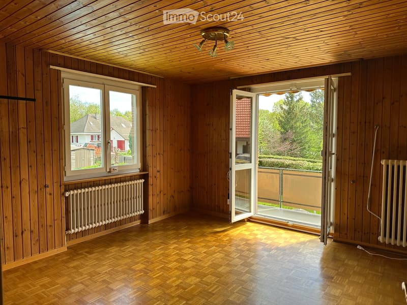 Empty room with wooden walls, wooden floor, large windows, and a sliding glass door leading to a balcony.