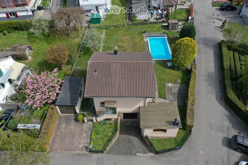 Aerial view of a two-story house with a tiled roof, surrounded by a well-maintained garden, a swimming pool, and a garage.
