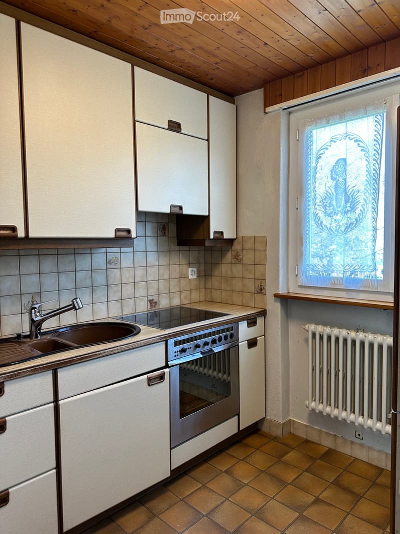 A cozy kitchen with white cabinets, a stainless steel oven, a sink with a faucet, and a radiator near the window.