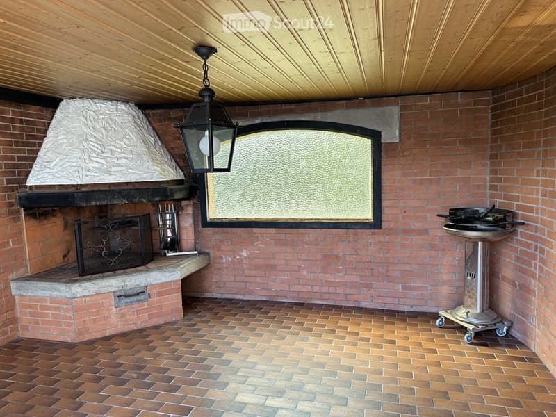 Brick outdoor area with a fireplace, grill, and chandelier.
