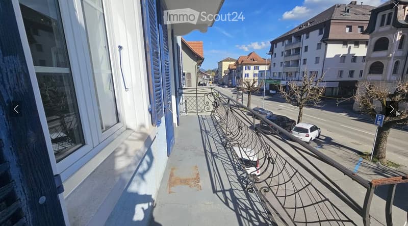 Balcony with metal railing overlooking a street lined with parked cars and buildings.