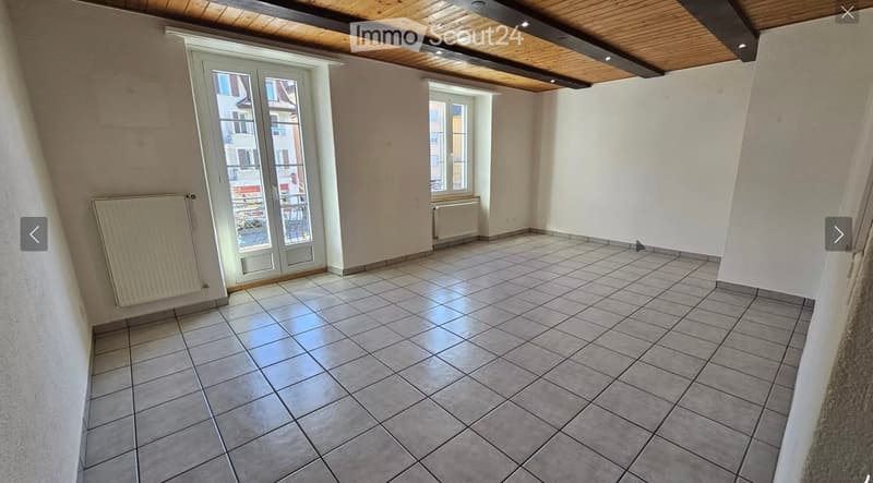 Empty room with tiled floor, white walls, large window, and radiator. No furniture or equipment present.