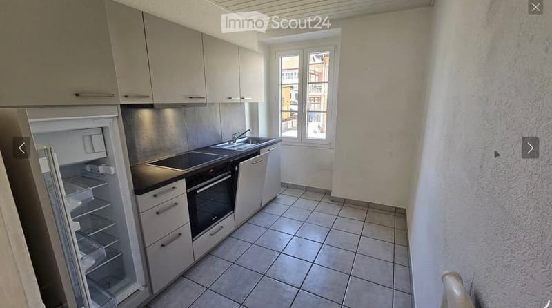 Modern kitchen with white cabinets, stainless steel appliances, tiled floor, and a window overlooking the street.