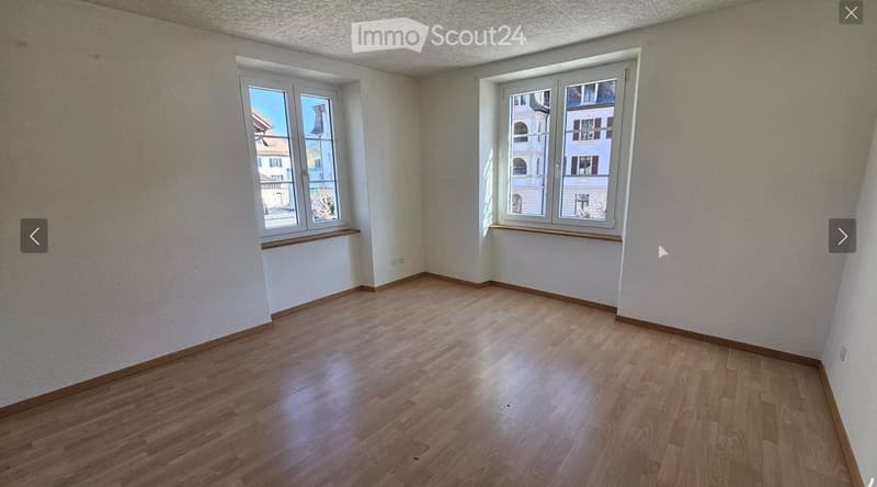 Empty room with wooden flooring, white walls, and two windows offering a view of the outside. No furniture or equipment is present.