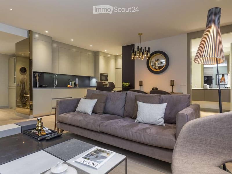 Modern living room with a grey sofa, coffee table, floor lamp, and a modern kitchen area with cabinets, a faucet, and a microwave.