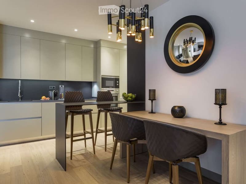 Modern kitchen and dining area with sleek cabinets, a central island, bar stools, and a round mirror on the wall.