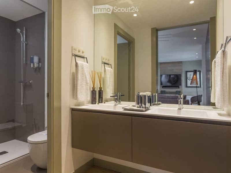 Modern bathroom with double sink, large mirror, towel racks, and a separate shower area with a toilet.