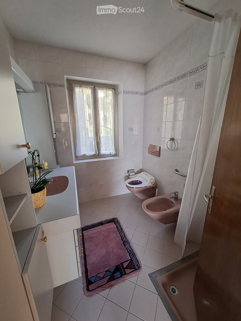 Bathroom with white tiles, a sink, a toilet, a bidet, a shower, and a window with curtains.