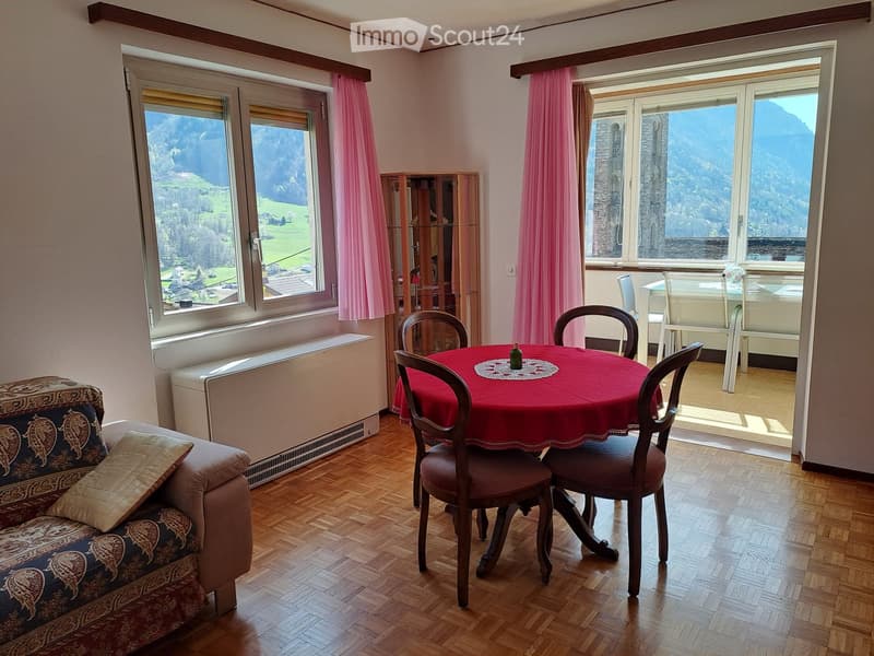 Dining area with a round table and chairs, a couch with a pillow, a cabinet, and windows with curtains