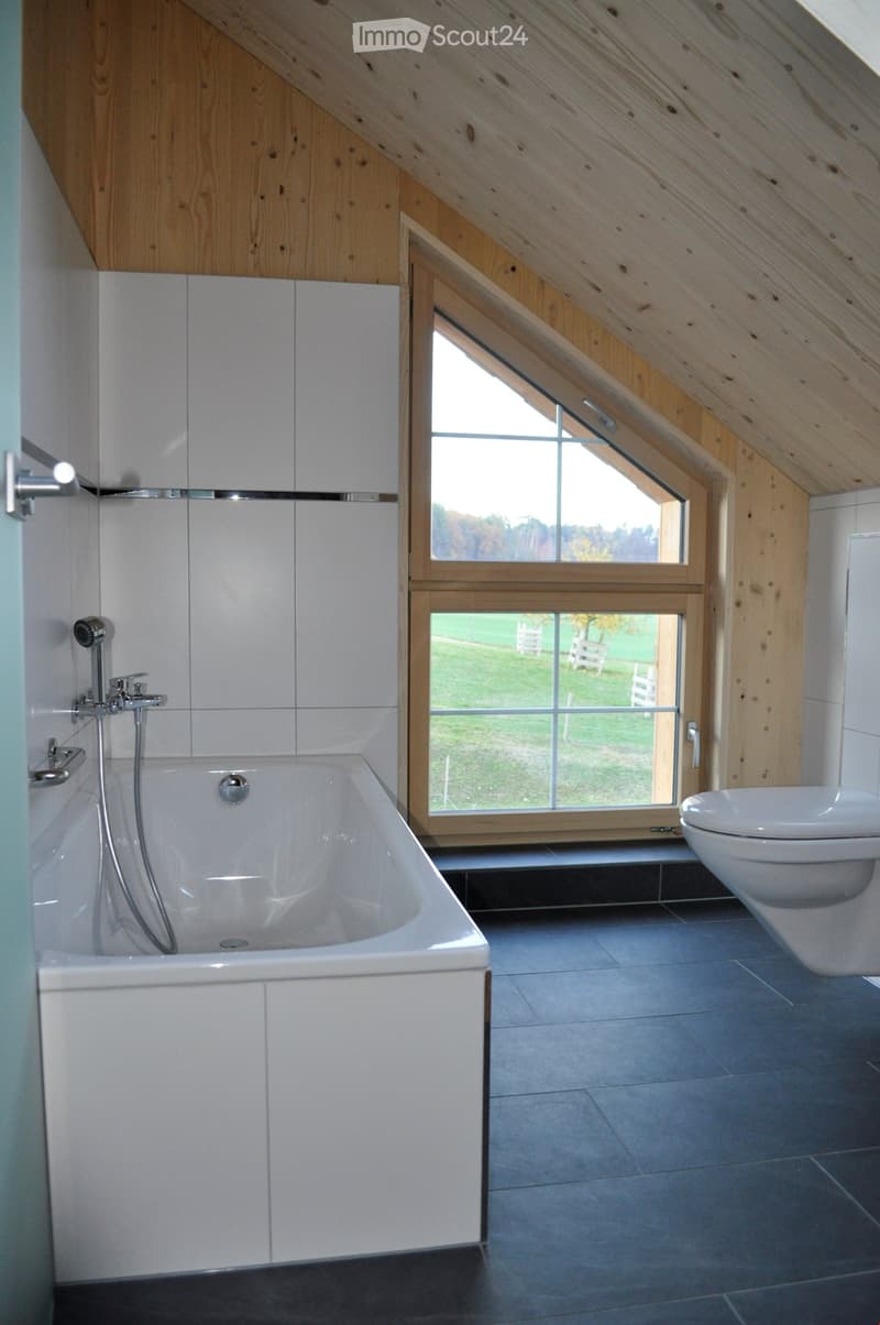 Modern bathroom with a large window, bathtub, toilet, and sleek fixtures.