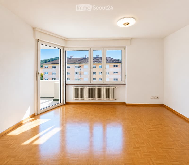 Empty room with wooden flooring, large windows, and a radiator. No furniture or equipment present.
