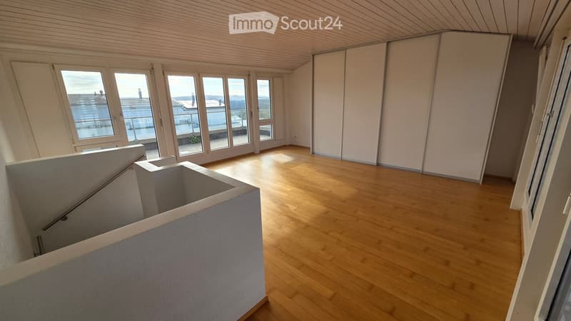 Empty room with wooden flooring, large windows, and a staircase leading to another level. No furniture or equipment present.