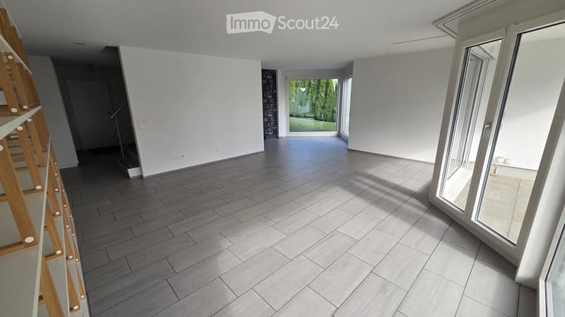 Empty room with grey tiled floor, white walls, large windows, and a staircase leading to another level.