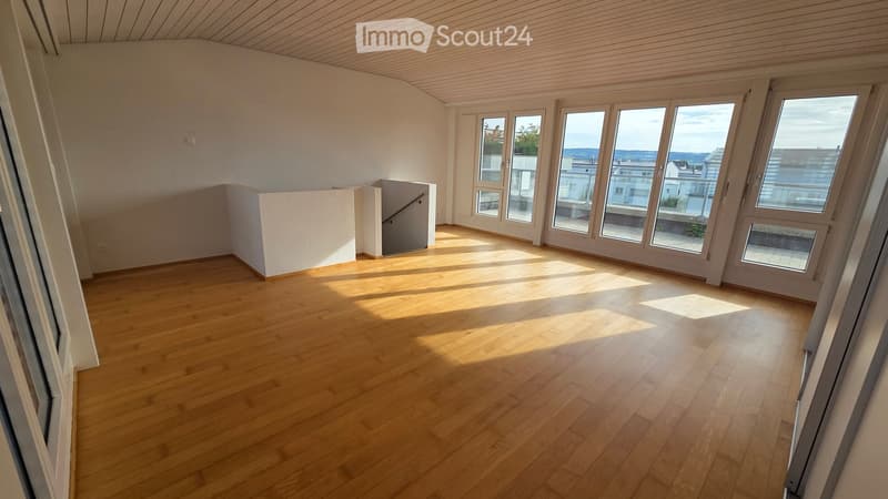 Empty room with wooden flooring, large windows, and a staircase leading to another level.