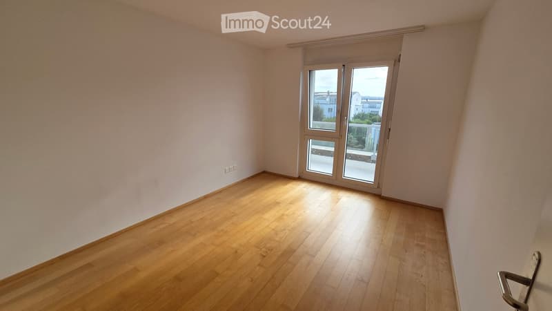 Empty room with wooden flooring and white walls, featuring a large sliding glass door leading to a balcony.