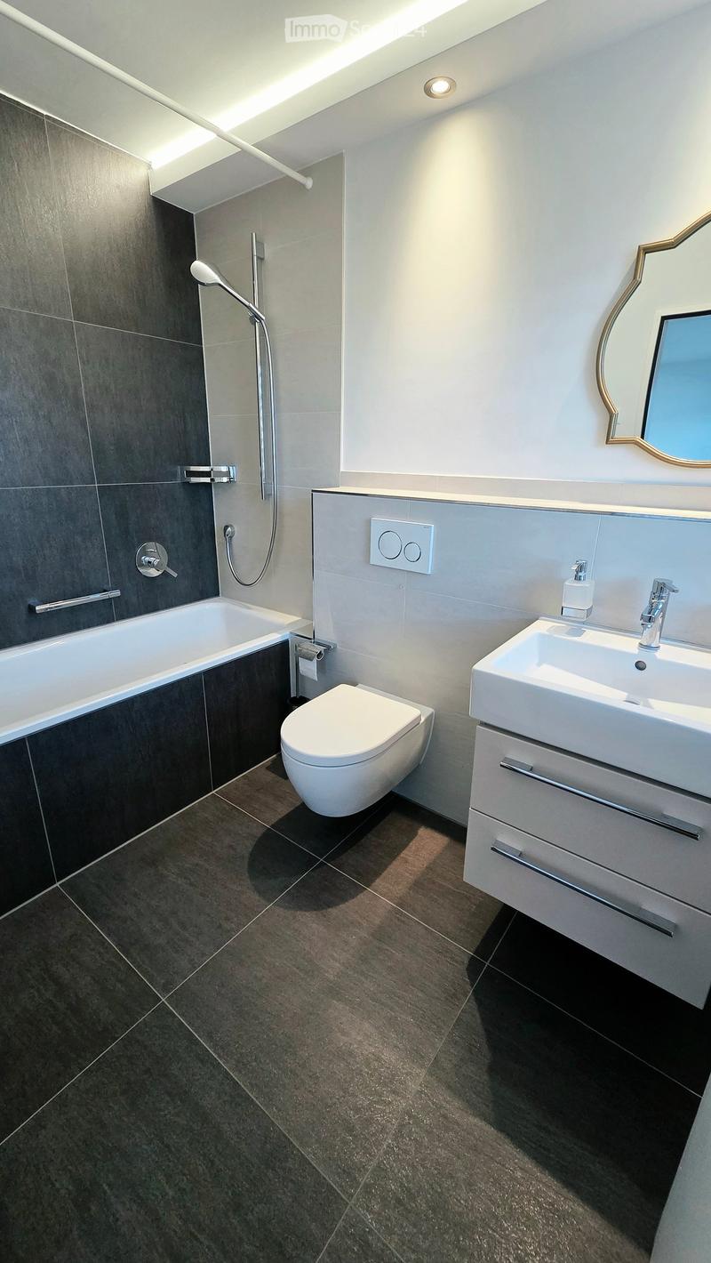 Modern bathroom with dark tiled walls and floor, featuring a bathtub, toilet, sink, and mirror.