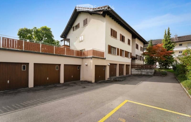 Two-story residential building with multiple garage doors, balconies, and a spacious driveway.