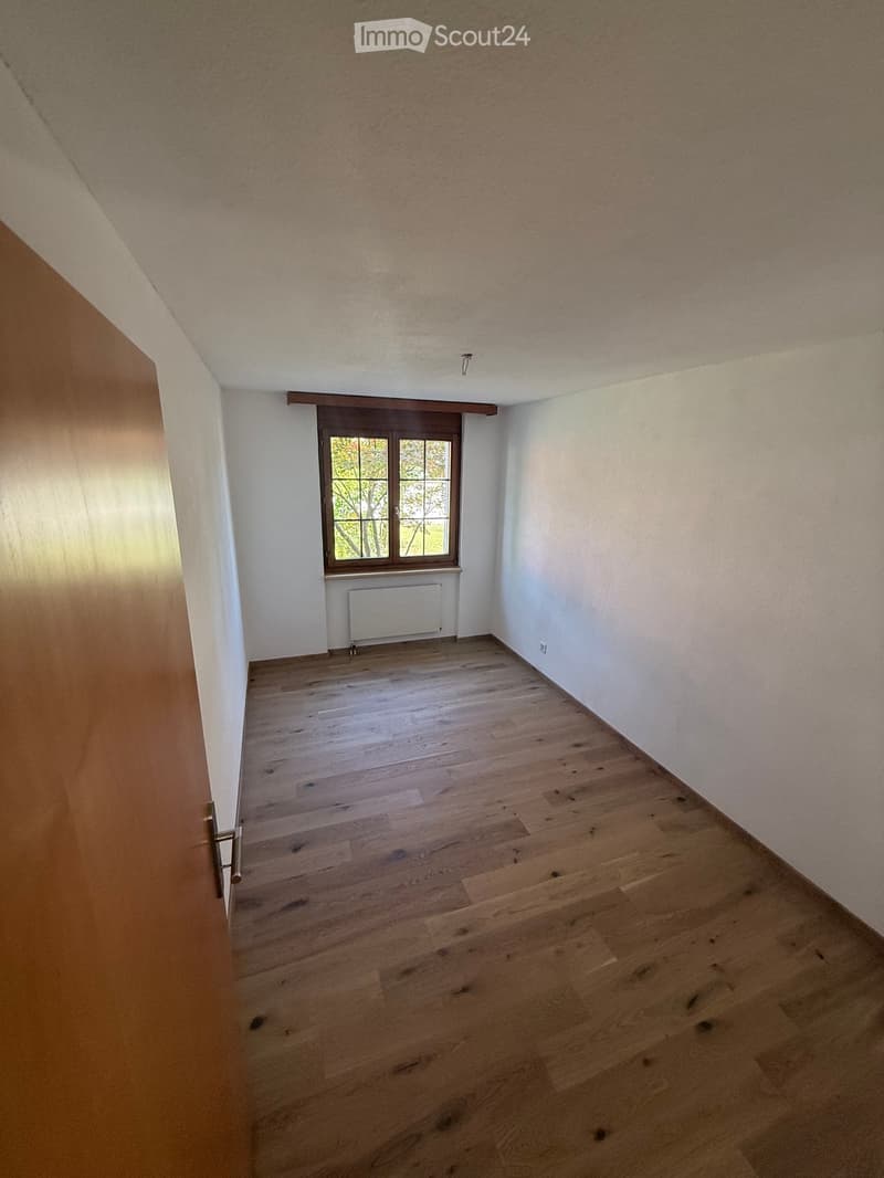 Empty room with wooden flooring, white walls, and a window with a radiator below it.