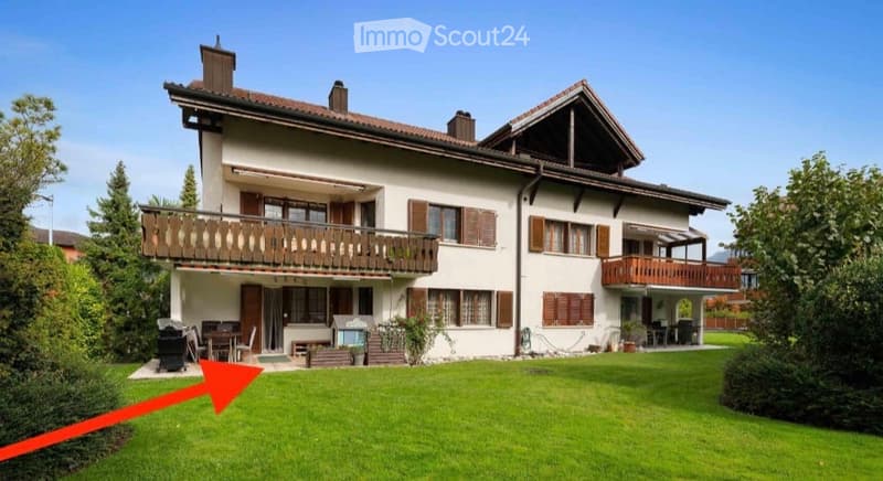 Two-story house with white walls, brown shutters, and balconies on both floors. The house features a well-maintained lawn and outdoor seating area.