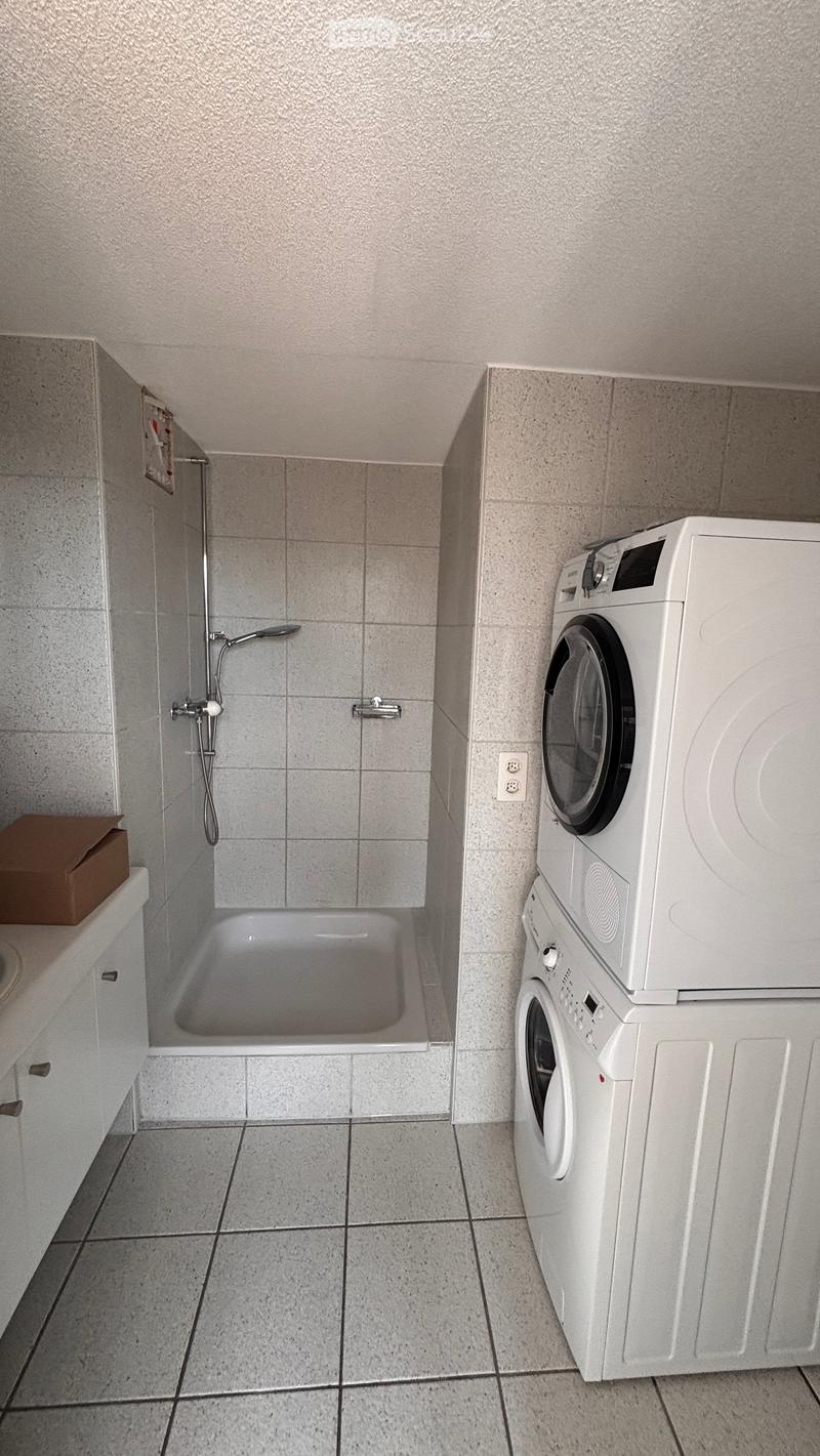 Bathroom with a bathtub, shower, and stacked washing machine and dryer.