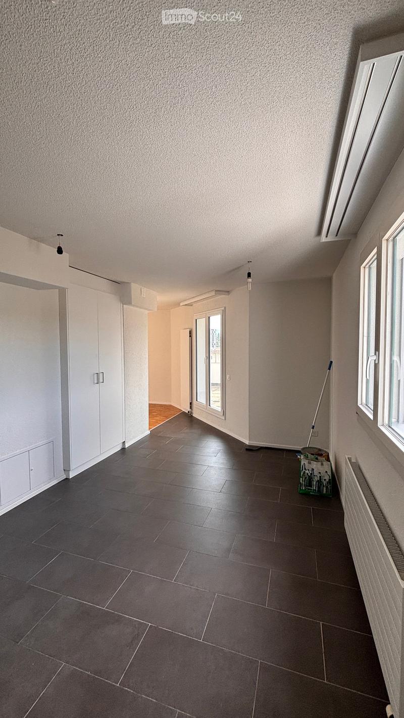 Empty room with dark tiled floor, white walls, and large windows. No furniture or equipment visible.