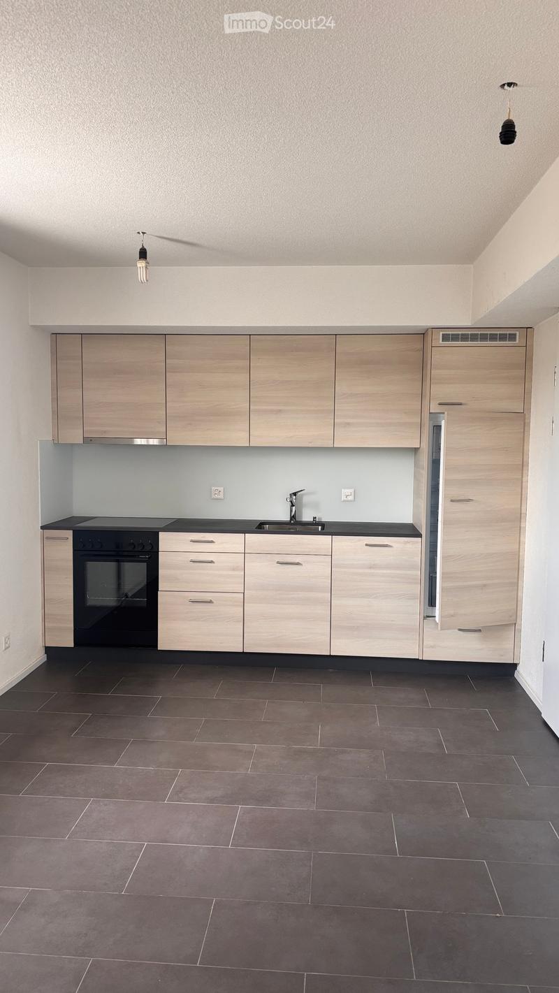 Modern kitchen with light wooden cabinets, black countertop, and dark tiled floor. Features an oven, sink, and faucet.