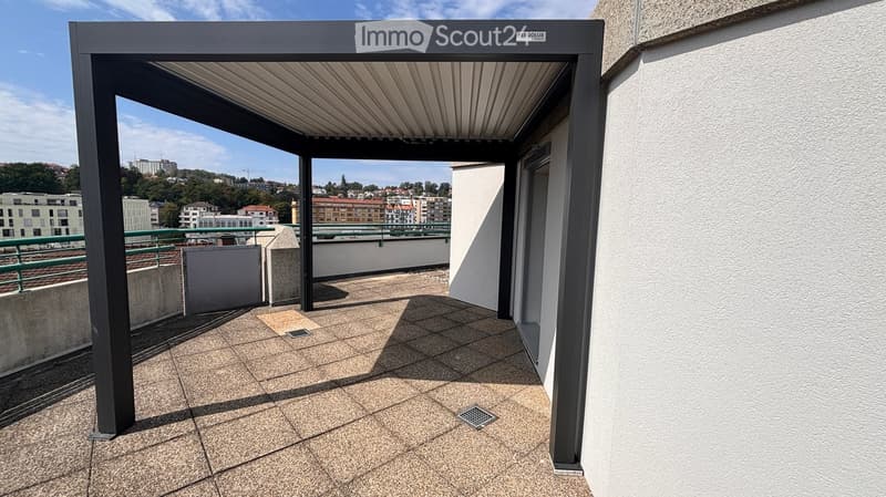 Covered balcony with tiled floor, metal frame, and open view of cityscape and surrounding buildings.