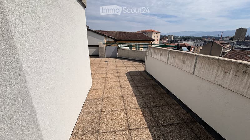 Balcony with tiled floor, low concrete railing, and a view of the cityscape and distant mountains.