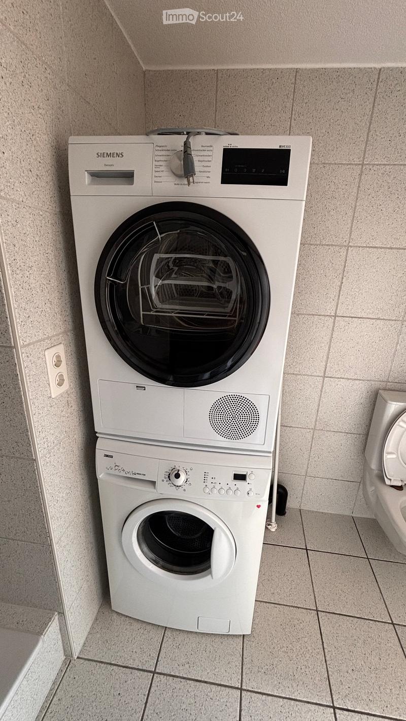 Bathroom with a white washing machine and dryer stacked vertically, and a toilet visible to the right.