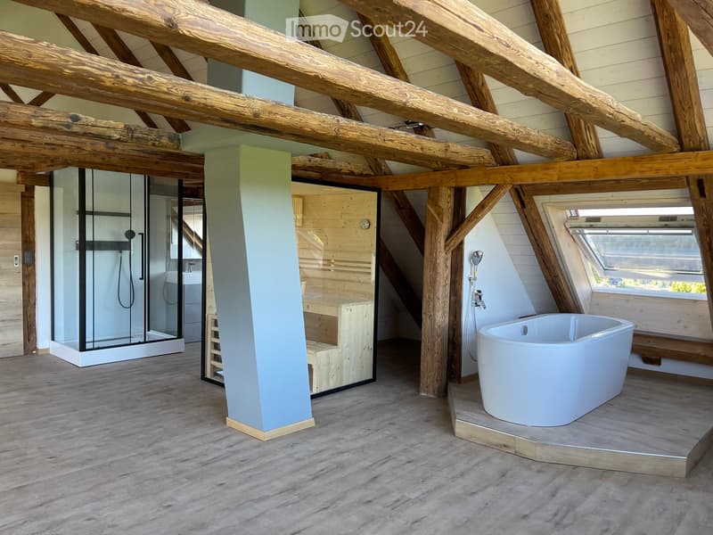 Modern bathroom with exposed wooden beams, a freestanding bathtub, a glass-enclosed shower, and a wooden stool.